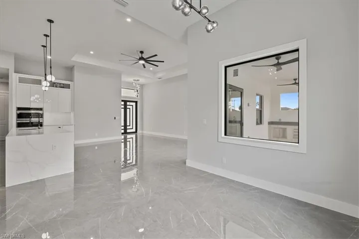 Unfurnished living room featuring a tray ceiling, light marble finish flooring, a chandelier, recessed lighting, and a ceiling fan