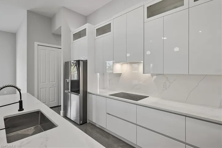 Kitchen featuring white cabinetry, glass insert cabinets, stainless steel fridge with ice dispenser, modern cabinets, and light stone countertops