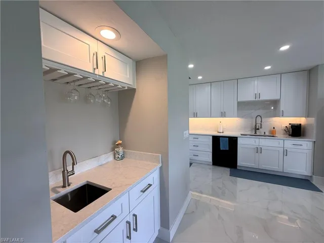 Kitchen with white cabinets, recessed lighting, black dishwasher, light stone countertops, and light marble finish floors