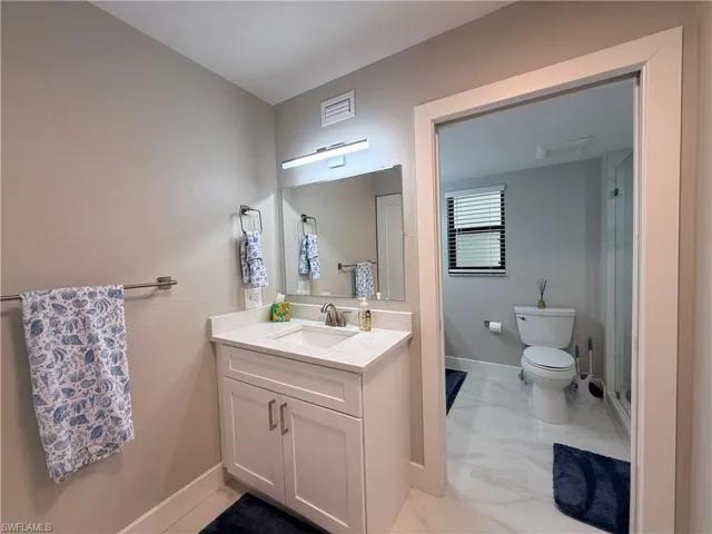 Full bath featuring vanity, light marble finish floors, and a shower stall