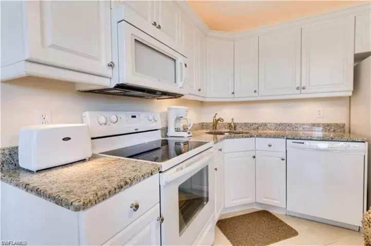 Kitchen with light tile patterned flooring, sink, white appliances, and white cabinets