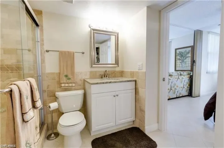 Bathroom with tile patterned flooring, walk in shower, toilet, vanity, and tile walls