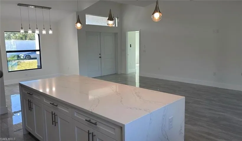 Kitchen with open floor plan, a kitchen island, pendant lighting, vaulted ceiling, and light stone counters