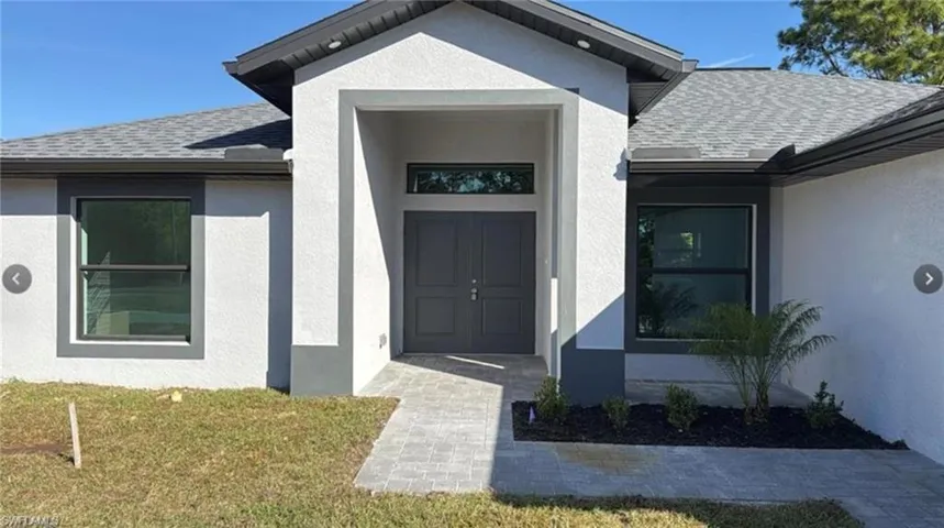 Doorway to property with roof with shingles, stucco siding, and a yard