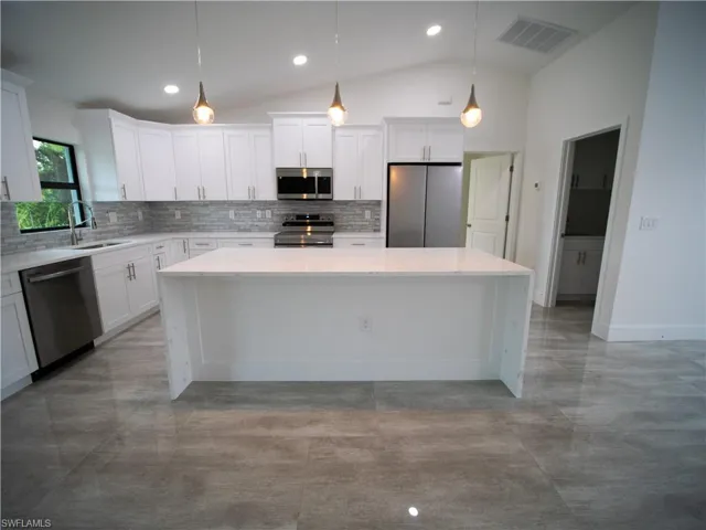 Kitchen featuring decorative backsplash, a spacious island, light stone counters, appliances with stainless steel finishes, and lofted ceiling
