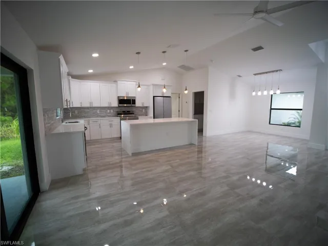 Kitchen with decorative backsplash, white cabinets, a center island, lofted ceiling, and stainless steel appliances