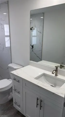 Bathroom with vanity, a marble finish shower, and dark wood-type flooring