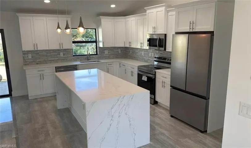 Kitchen with appliances with stainless steel finishes, white cabinetry, decorative light fixtures, a kitchen island, and light stone countertops