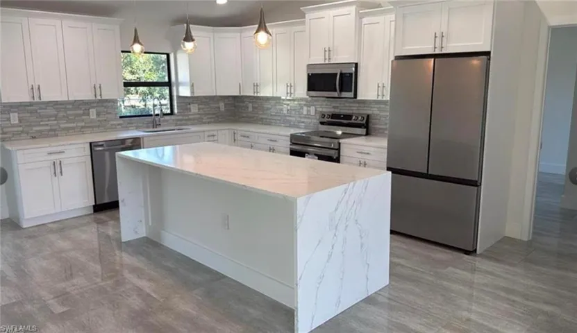 Kitchen featuring appliances with stainless steel finishes, white cabinets, a center island, and light stone counters