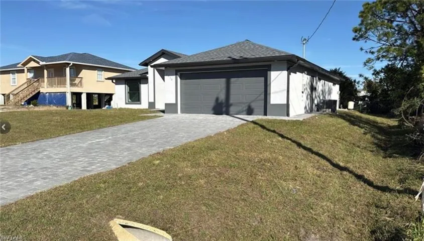 Rear view of house with stucco siding, decorative driveway, a yard, and an attached garage