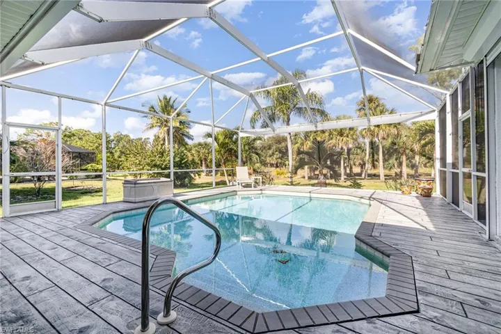 View of pool with a hot tub, a wooden deck, and a lanai