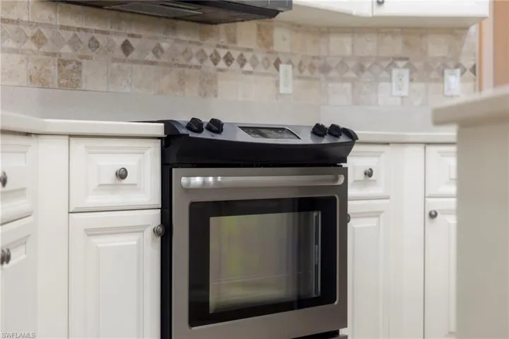Kitchen view of electric stove, light countertops, tasteful backsplash, and white cabinets