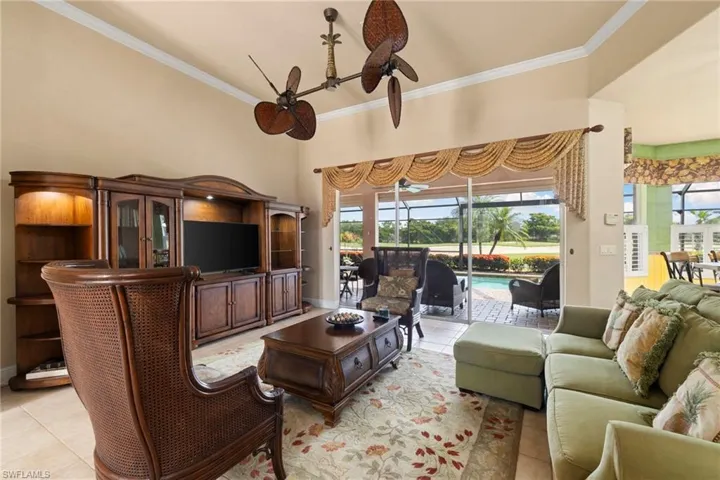 Living room with ceiling fan, light tile patterned floors, and crown molding has sliding glass doors that lead out to the pool and large screened lanai area.