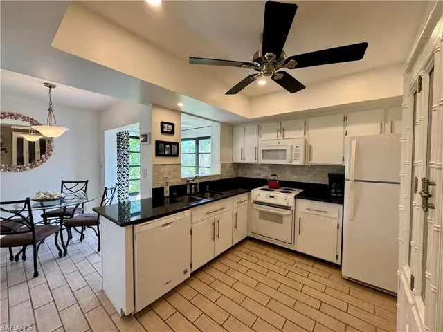 Kitchen with hanging light fixtures, white appliances, white cabinets, sink, and tasteful backsplash