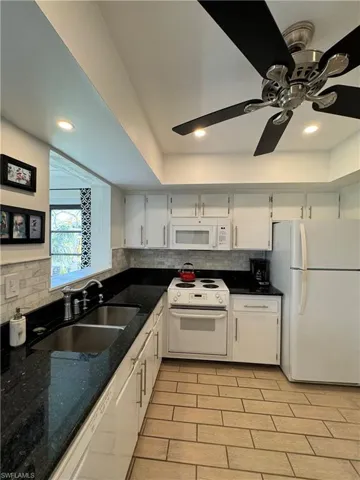 Kitchen featuring white appliances, sink, white cabinetry, and ceiling fan