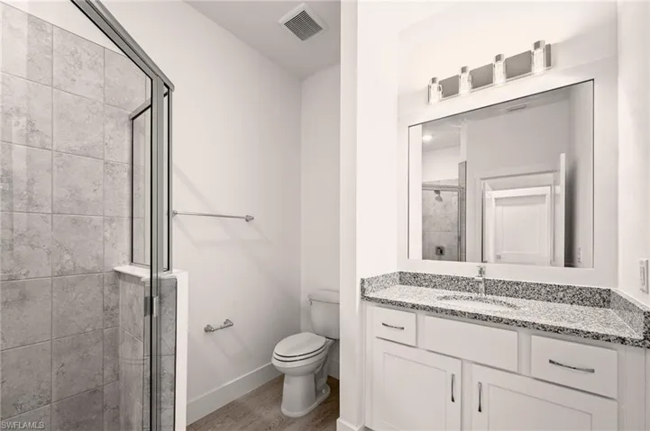 Bathroom with visible vents, toilet, a stall shower, wood finished floors, and baseboards