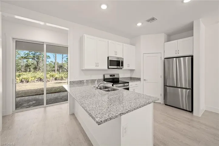 Kitchen with light stone counters, visible vents, a sink, white cabinets, and appliances with stainless steel finishes