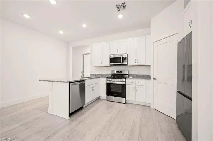 Kitchen featuring light wood-type flooring, visible vents, white cabinetry, stainless steel appliances, and a peninsula