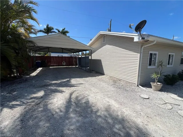 View of side of property featuring a detached carport, fence, and gravel driveway
