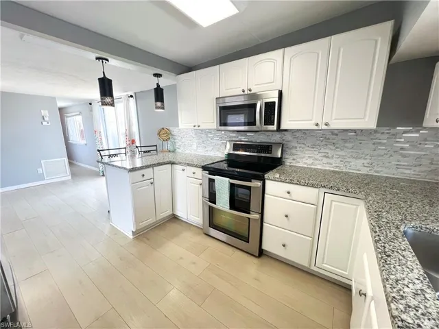 Kitchen featuring white cabinetry, a peninsula, stainless steel appliances, visible vents, and decorative backsplash