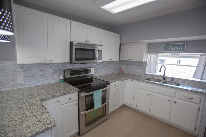 Kitchen featuring a sink, backsplash, white cabinetry, light stone countertops, and appliances with stainless steel finishes