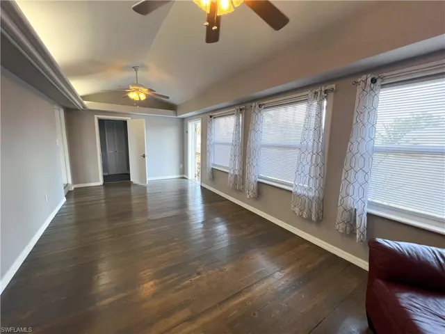 Unfurnished room featuring dark wood finished floors, plenty of natural light, lofted ceiling, and ceiling fan