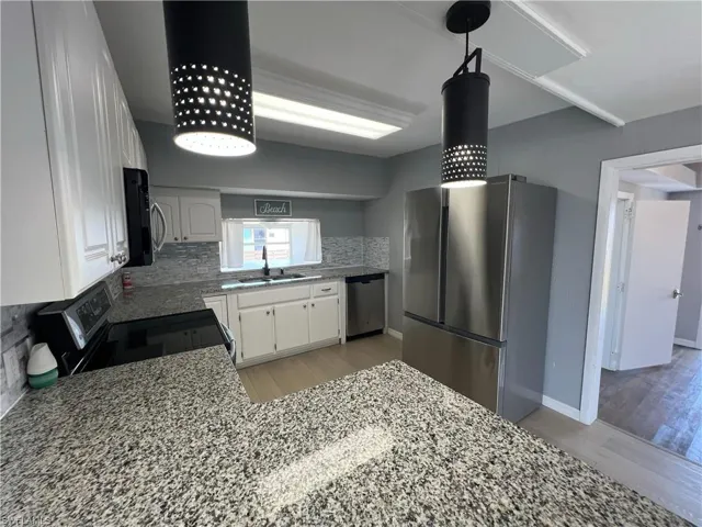 Kitchen with a sink, stainless steel appliances, white cabinets, light wood-style floors, and decorative backsplash