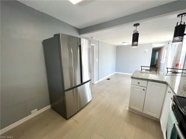 Kitchen with white cabinets, pendant lighting, freestanding refrigerator, light wood-style flooring, and range with electric cooktop