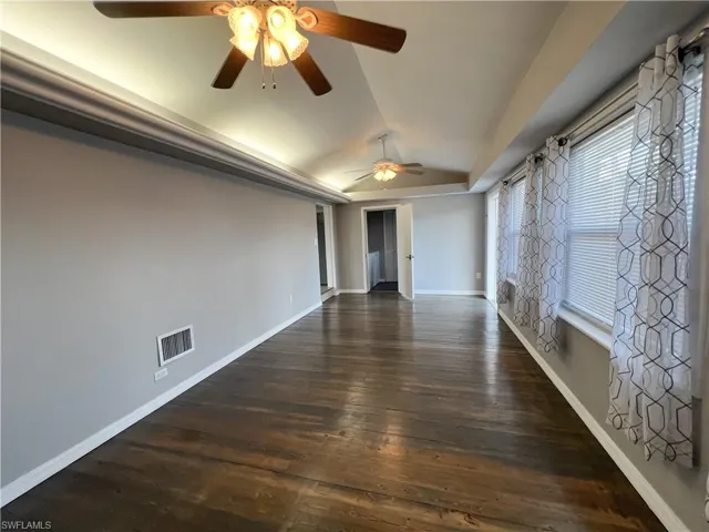 Spare room with visible vents, baseboards, ceiling fan, lofted ceiling, and dark wood-style floors