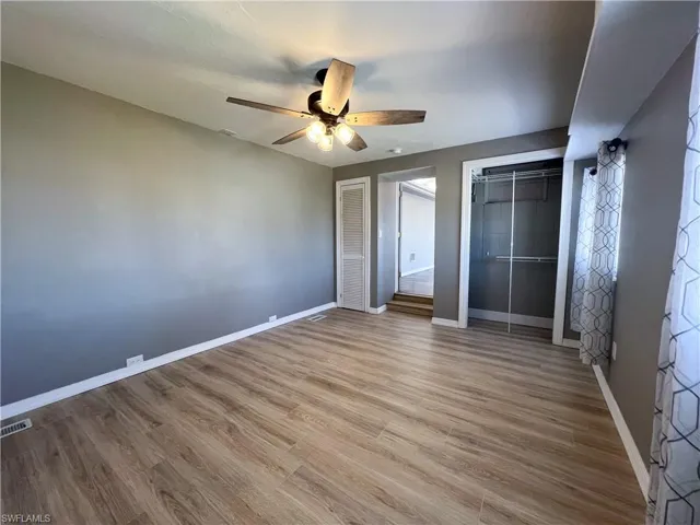 Unfurnished bedroom featuring multiple closets, visible vents, baseboards, wood finished floors, and a ceiling fan