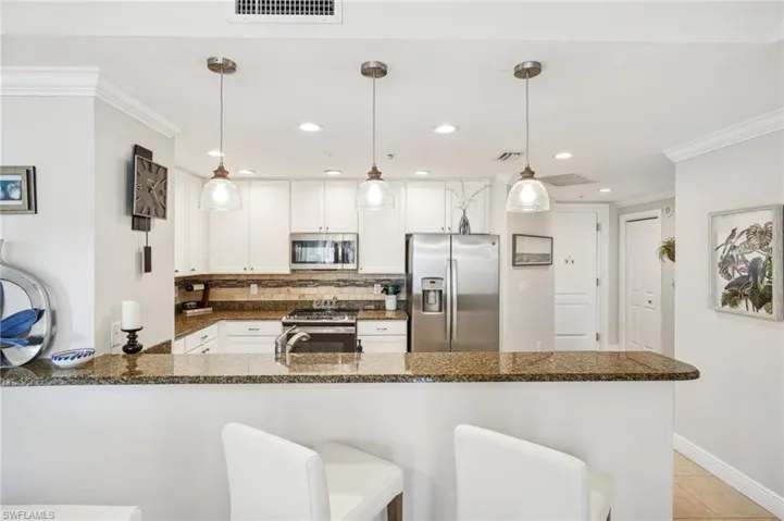 Kitchen with hanging light fixtures, white cabinetry, kitchen peninsula, and stainless steel appliances