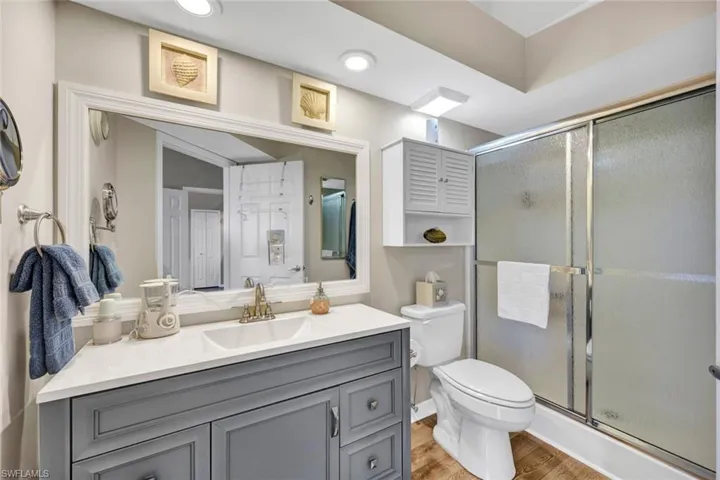 Bathroom with vanity, toilet, a shower with shower door, and wood-type flooring