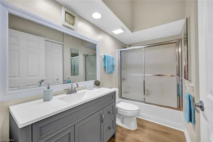 Full bathroom featuring vanity, toilet, wood-type flooring, and bath / shower combo with glass door