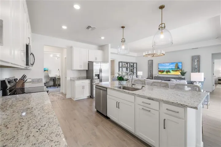 Kitchen featuring appliances with stainless steel finishes, a kitchen island with sink, white cabinets, and decorative light fixtures