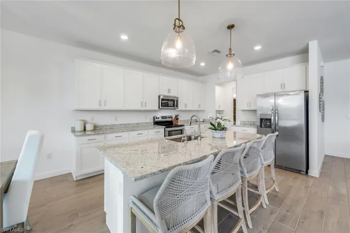 Kitchen featuring appliances with stainless steel finishes, a kitchen island with sink, white cabinets, and decorative light fixtures