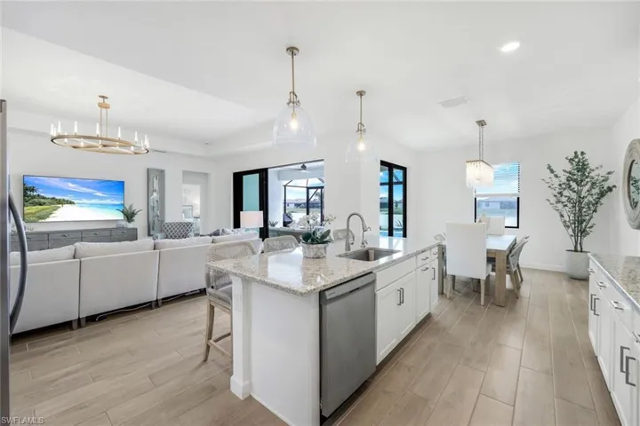 Kitchen featuring appliances with stainless steel finishes, a kitchen island with sink, white cabinets, and decorative light fixtures