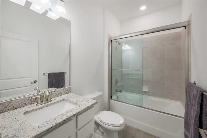 Full bathroom featuring vanity, shower / bath combination with glass door, and toilet