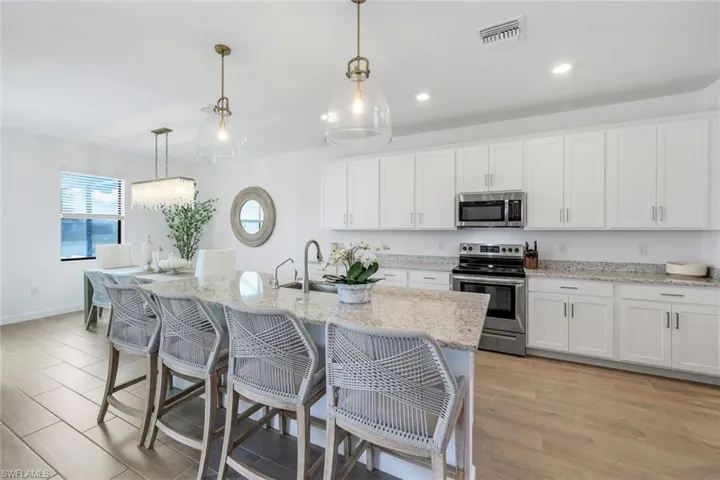 Kitchen featuring appliances with stainless steel finishes, a kitchen island with sink, white cabinets, and decorative light fixtures