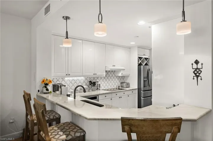Kitchen featuring white cabinetry, light-toned countertops, a patterned tile backsplash, stainless steel appliances, and pendant lighting