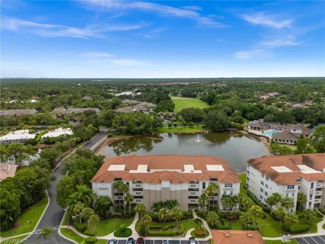Multi-story building featuring a tile roof, surrounded by mature landscaping, a pond with a fountain, and a paved parking area