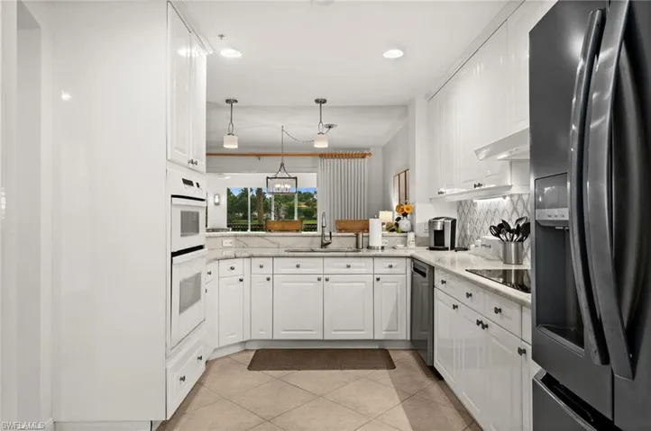 White cabinetry with dark hardware, built-in double ovens, light-toned tile flooring, and a patterned backsplash