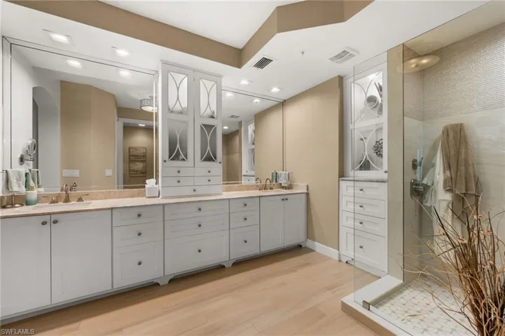 Dual vanity with undermount sinks, expansive mirrors, wood-finish flooring, and a glass-enclosed shower