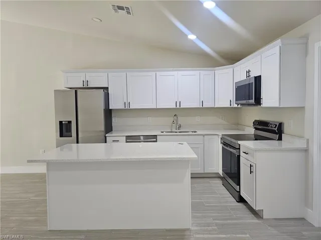 Kitchen featuring appliances with stainless steel finishes, white cabinetry, light stone counters, vaulted ceiling, and recessed lighting