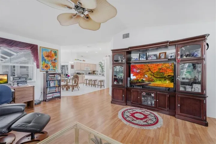 Living room with ceiling fan, light wood finished floors, and vaulted ceiling
