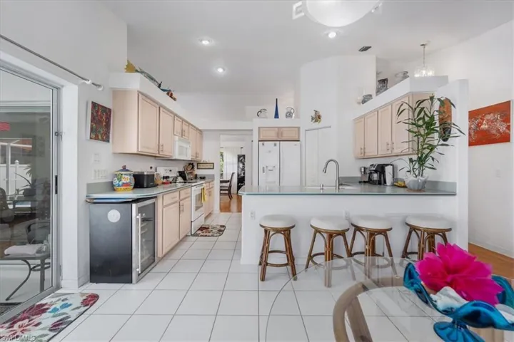 Kitchen featuring a peninsula, white appliances, a breakfast bar, beverage cooler, and light tile patterned floors