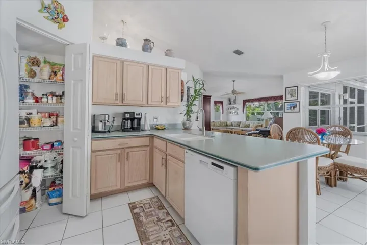 Kitchen featuring light brown cabinetry, white appliances, light tile patterned floors, a ceiling fan, and a peninsula