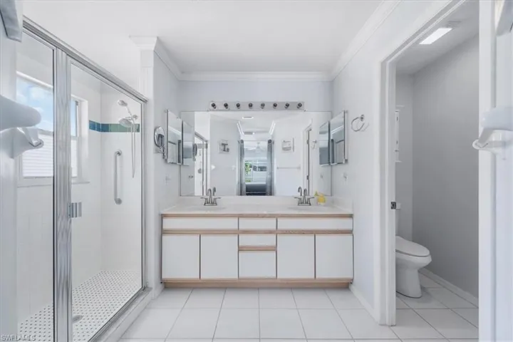 Bathroom with a shower stall, double vanity, tile patterned flooring, and ornamental molding