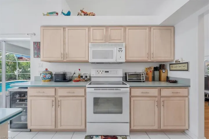 Kitchen featuring light brown cabinetry, white appliances, and wine cooler