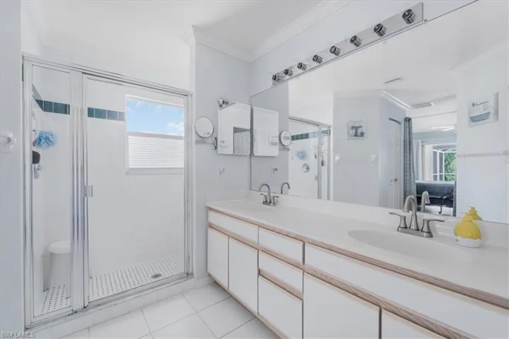Full bath with a stall shower, crown molding, healthy amount of natural light, double vanity, and tile patterned flooring