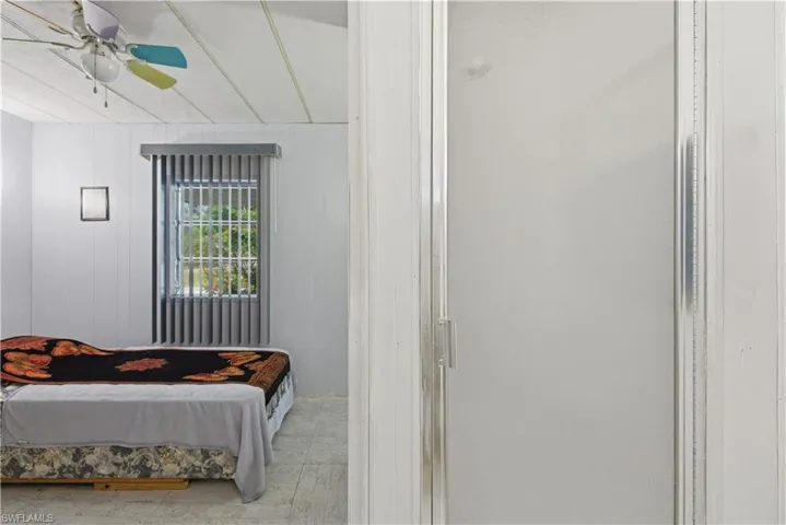 Room with paneled walls, a window featuring vertical blinds, and a ceiling fan